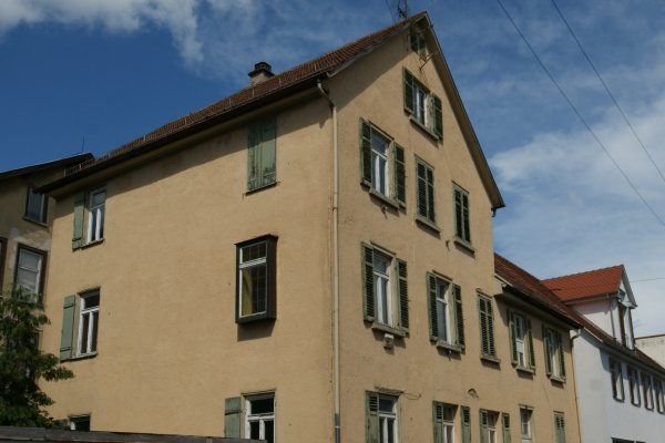 Ockerfarbenes Mehrfamilien-Eckhaus mit schmutzig-grünen Fensterläden